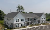 A large white and grey building with a parking lot in front.