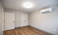 A room with a white ceiling, a white air conditioner, and three white doors at Hudson Heights Apartments, Mechanicville, NY