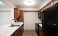 A kitchen with a black refrigerator and wooden cabinets at Hudson Heights Apartments, Mechanicville, NY