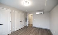 A room with a white ceiling, a wood floor, and a white wall with a door on the left at Hudson Heights Apartments, Mechanicville, NY