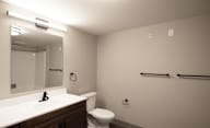 A bathroom with a toilet, sink, mirror, and towel racks at Hudson Heights Apartments, Mechanicville, NY