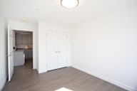A kitchen with white cabinets and a white fridge is visible through the open door.