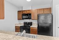 A kitchen with a black refrigerator, microwave, and oven.