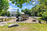 A playground with a slide and a wooden structure surrounded by a fence.