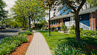A tree-lined sidewalk in front of a brick house.