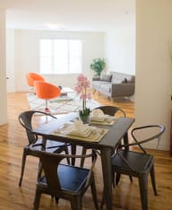 a bright and airy living room with a black dining table and orange chairs