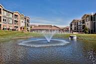 A fountain in the middle of a pond in front of apartment buildings.