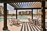 A wooden pergola over a pool with chairs underneath.