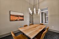A wooden table is surrounded by chairs in a room with a large picture hanging on the wall.