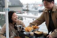 A man is serving food to a woman and her dog at a restaurant.