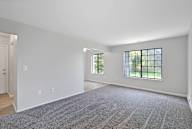 A large, empty room with a carpeted floor and two windows.