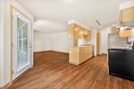 an empty living room and kitchen with wood flooring and a door to the kitchen