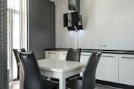 A white dining table with two black chairs in a modern kitchen.