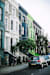 A street with cars parked on the side and a green tree in front of a building.