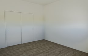 A room with a brown floor and three white doors.