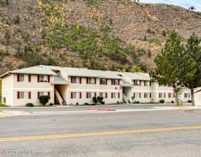 Apartment building with a red trim on the front is in front of a mountain.