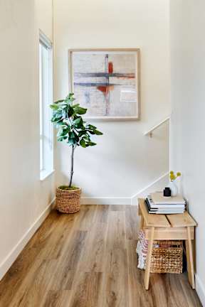 a living room with wooden floors and a plant and a painting on the wall