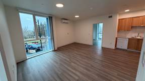 A spacious room with wooden flooring and a kitchen area in the background.