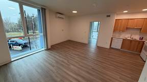 A spacious room with wooden flooring and a kitchen area in the background.