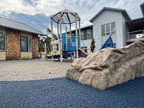 A playground with a large rock in the foreground and a swing set in the background.