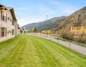 A long grassy lawn leads to a house with a mountain in the background.