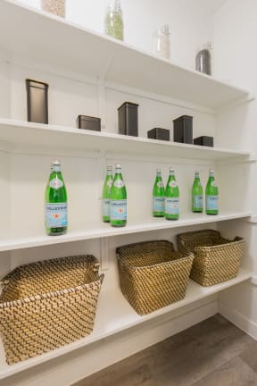 a pantry with white shelves and wicker baskets and green bottles of soda on the shelves