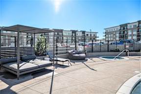 a rooftop patio with lounge chairs and a pool and a building in the background