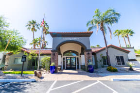 a building with a sign that reads leasing office in front of a palm tree