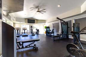 a large fitness room with exercise equipment and a ceiling fan