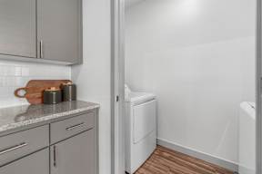 A kitchen with a white dishwasher and grey cabinets.