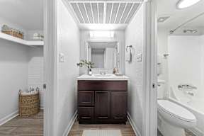 A white bathroom with a brown vanity and a white tub.
