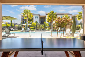 a ping pong table sits in front of a pool with palm trees in the background