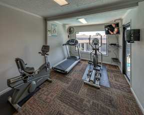 A gym room with a treadmill, elliptical trainer and a stationary bike.