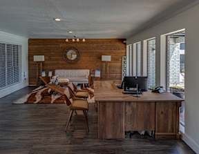 A wooden desk with a computer on it in a room with a clock on the wall.