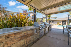 an outdoor kitchen with a barbecue and a pool in the background