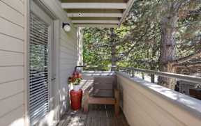 A wooden bench sits on a porch with a red vase and a tree in the background.