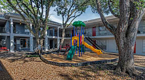 A playground with a green slide and a yellow slide in front of a building.