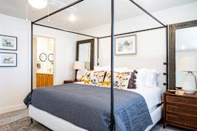A bedroom with a four poster bed and a nightstand with a lamp.