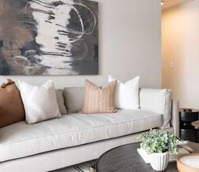 A living room with a white couch and a large abstract painting above it.