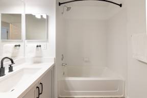 A white bathroom with a tub, sink, and mirror.