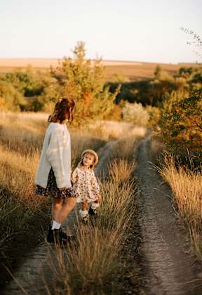 A woman and a child are walking down a path in a field.