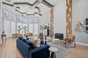 A residential lounge area with a blue couch, brown chairs, and a chandelier at Bardin Greene apartments in South Arlington, TX.