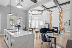 A residential lounge area with chairs, tables, a couch, and a kitchen island at Bardin Greene luxury apartments in Arlington, TX.