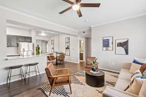 An open living room with a couch, chairs, and a ceiling fan, with views of a kitchen at Bardin Greene Arlington, TX apartments.