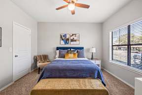 A bedroom with a bed, a ceiling fan, and a large window at Bardin Greene apartments in Arlington, Texas.