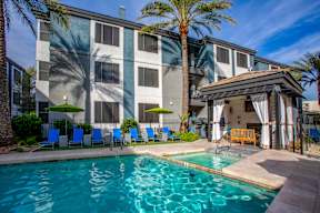A pool area with a building in the background and a palm tree in the foreground.