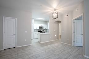 A spacious room with a kitchen in the background and a light hanging from the ceiling.