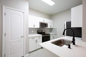 A kitchen with white cabinets and a black refrigerator.