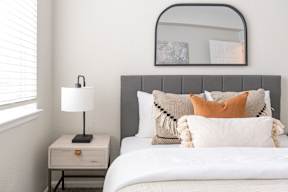 A bed with a white comforter and a grey headboard with a white nightstand and a lamp on it.