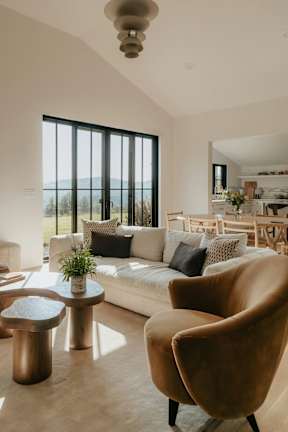A modern living room with a large window, a white sofa, and a wooden chair.